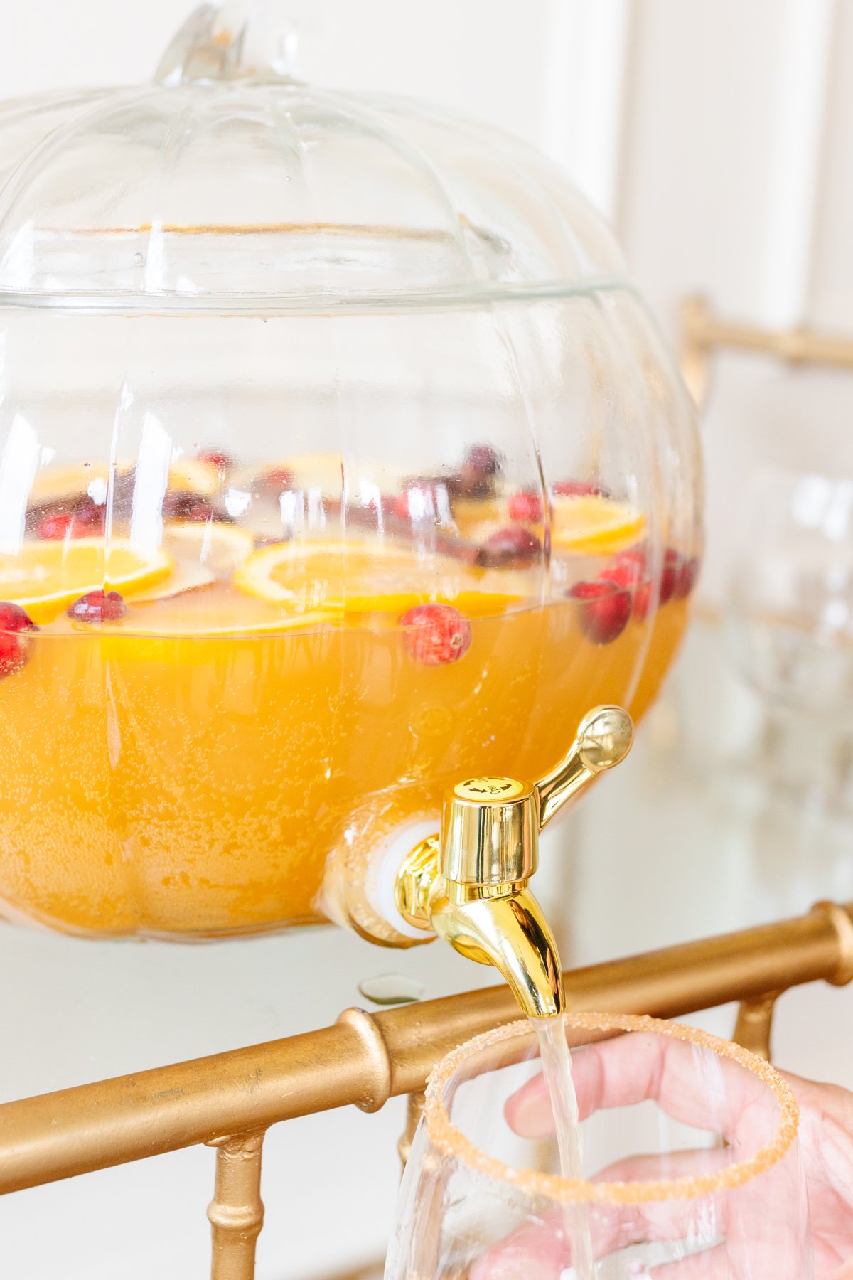 A clear glass pumpkin drink dispenser filled with apple cider sangria.