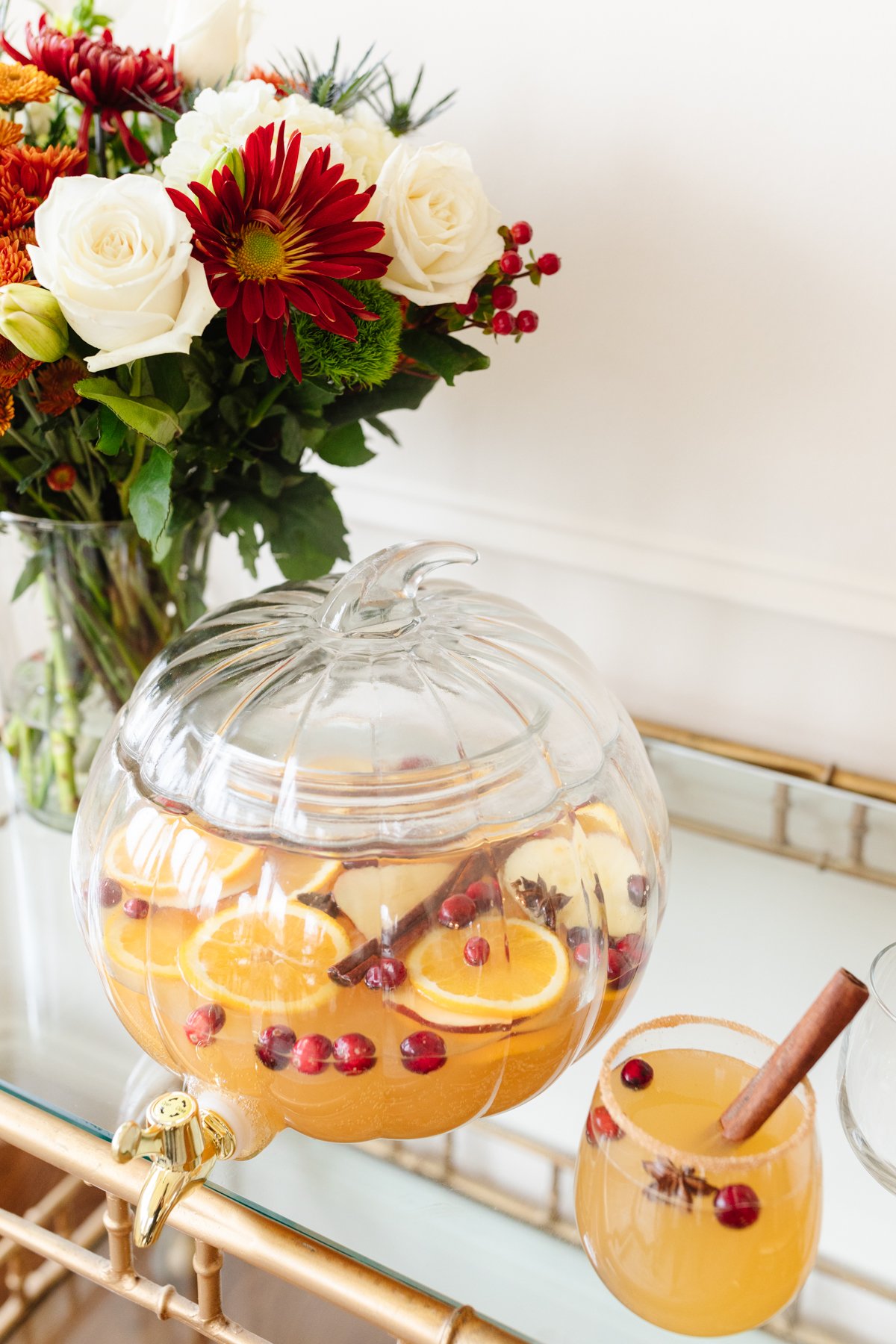 A clear glass pumpkin drink dispenser filled with apple cider sangria.