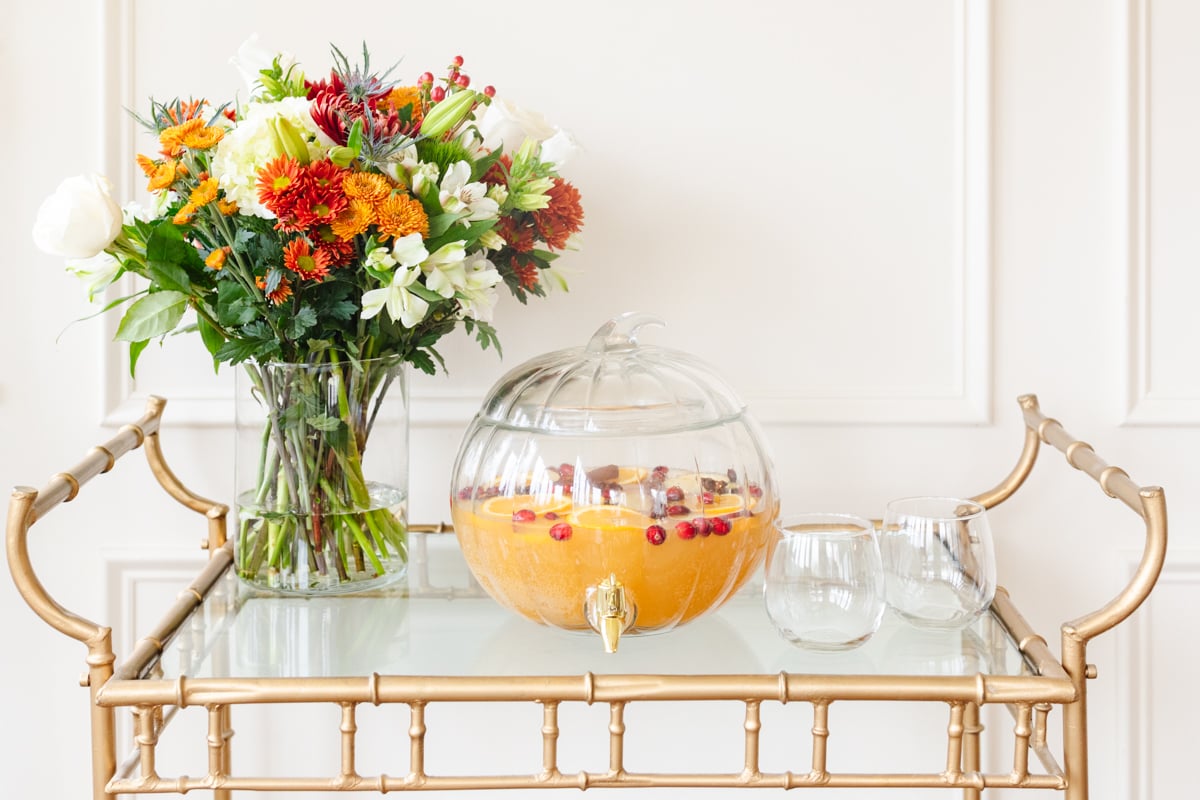 A clear glass pumpkin drink dispenser filled with apple cider sangria.