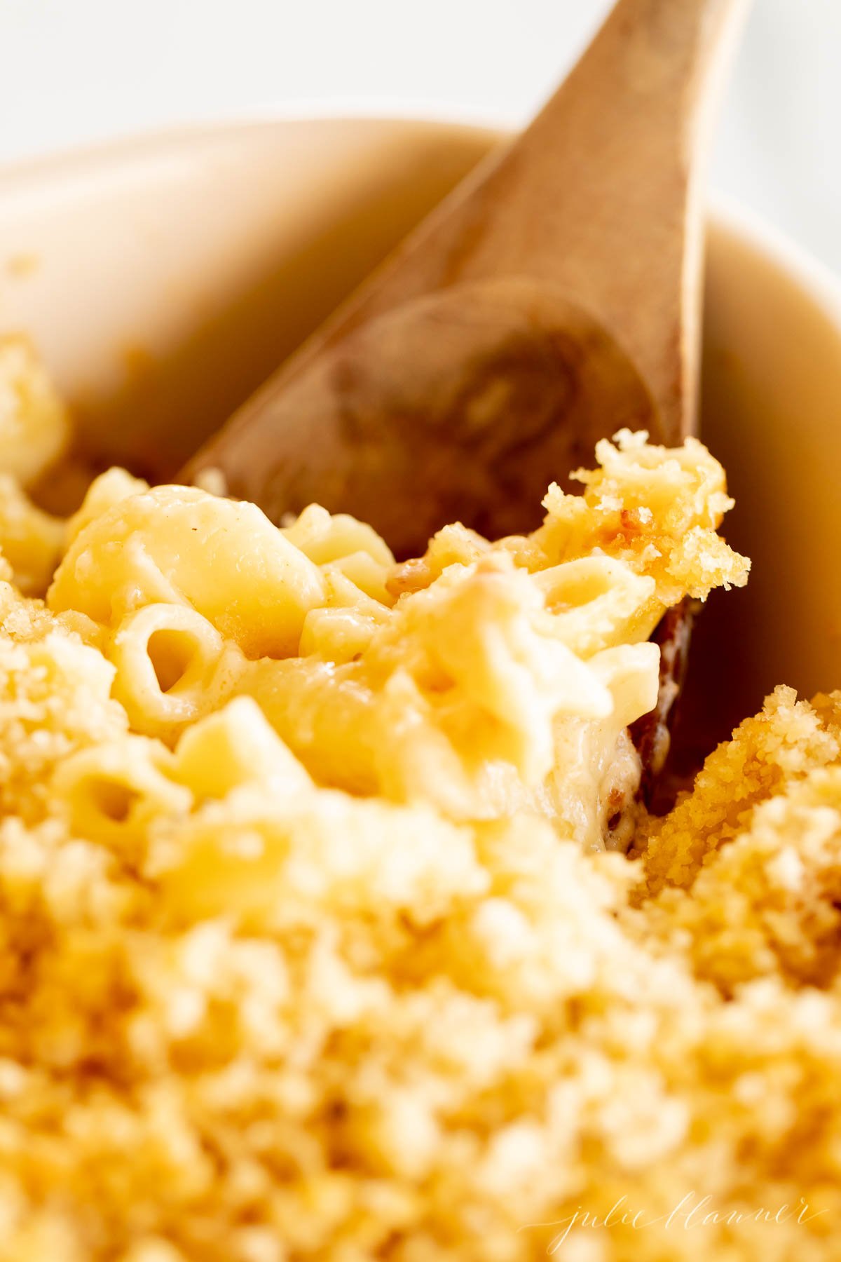 bacon mac and cheese in a white baking dish, with a wooden spoon in the corner.