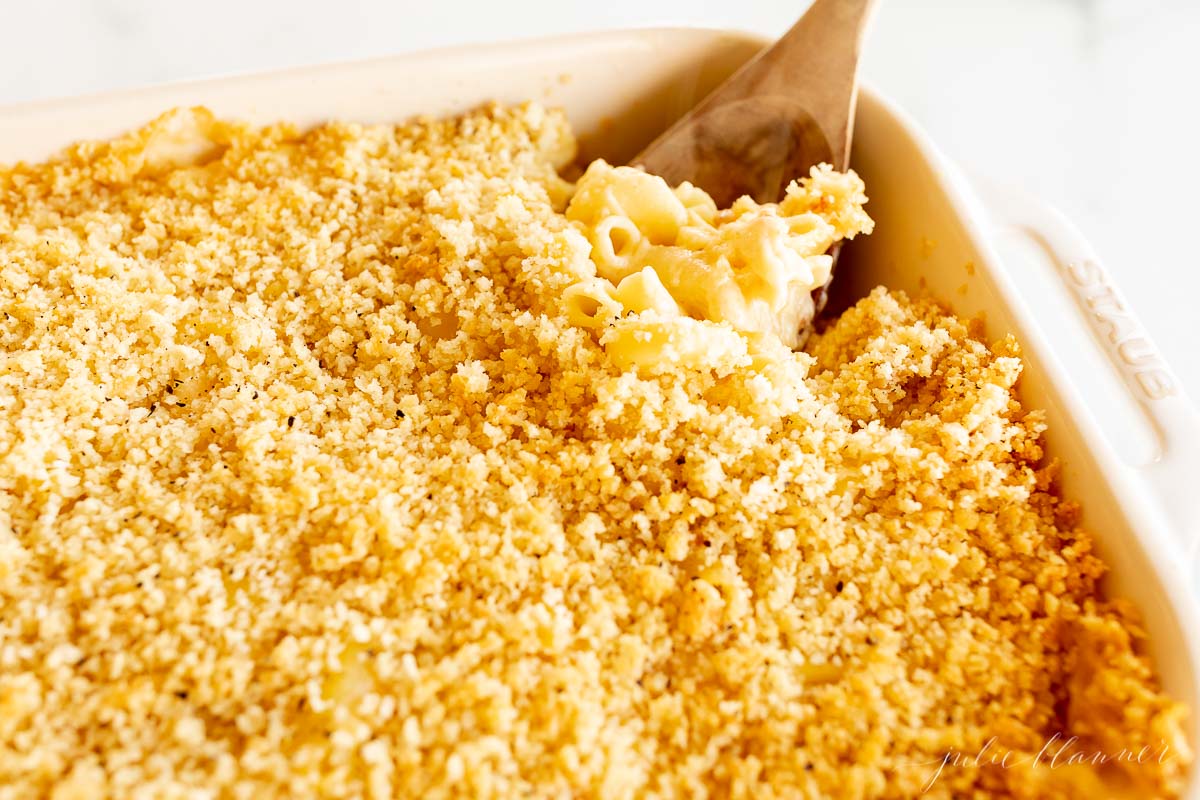 Bacon mac and cheese in a white baking dish with a wooden spoon.