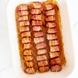 A white baking dish lined with bacon wrapped brown sugar little smokies.