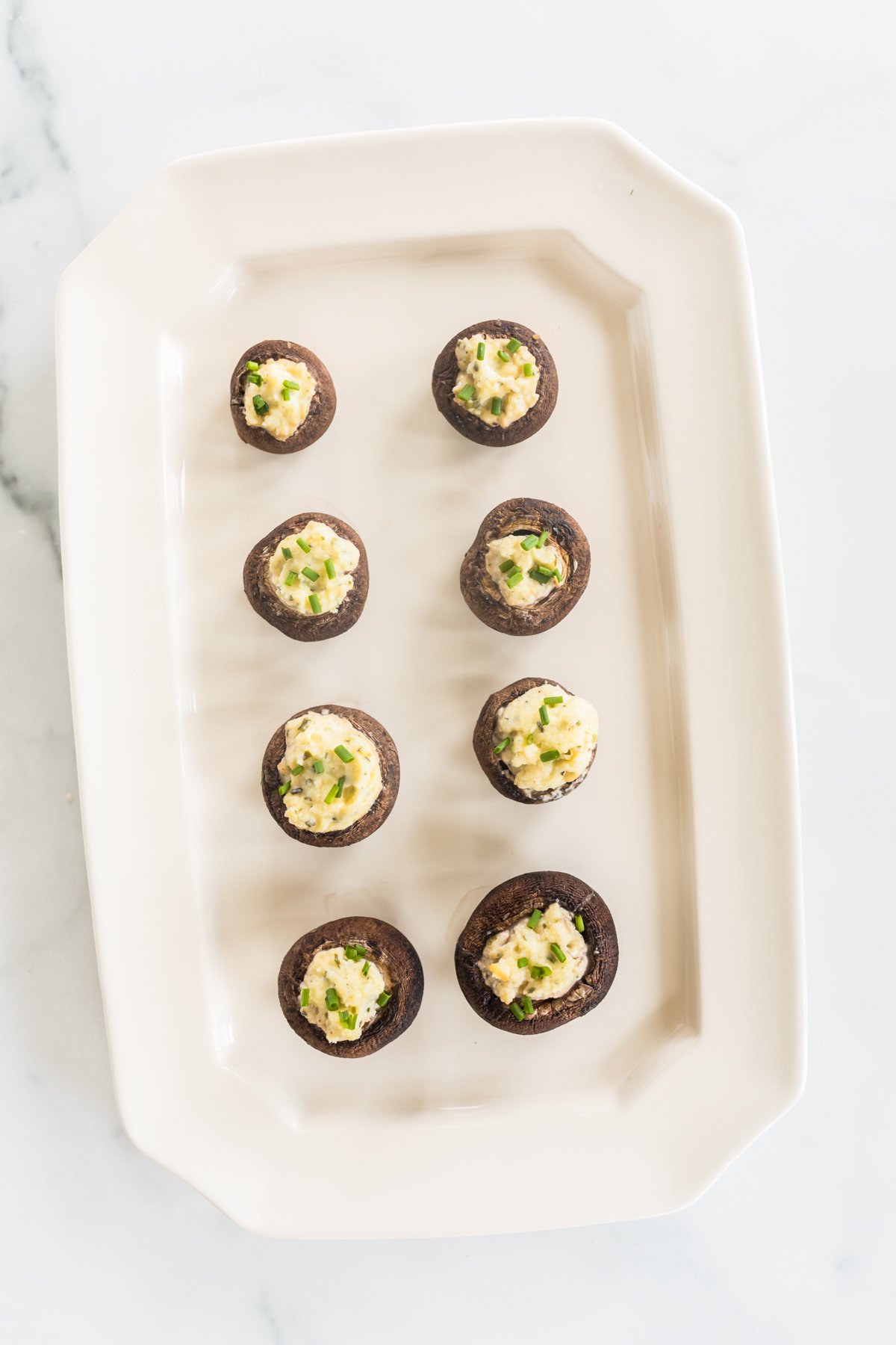 A white platter full of Boursin stuffed mushrooms.