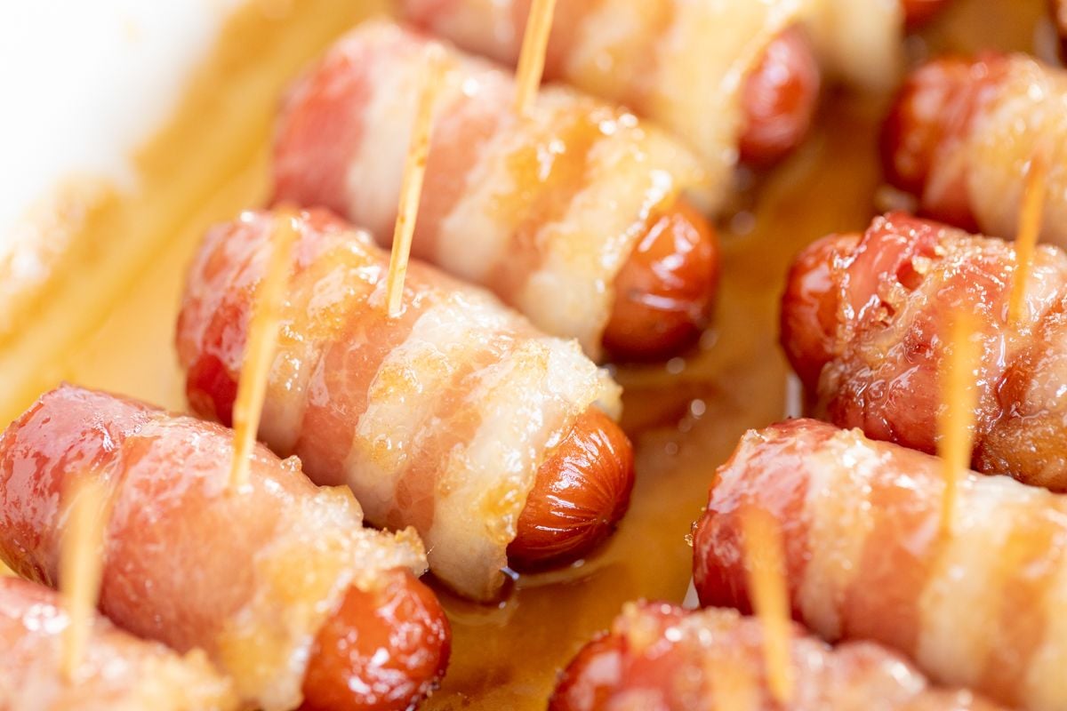 A white tray with bacon wrapped little smokies, each with a toothpick.