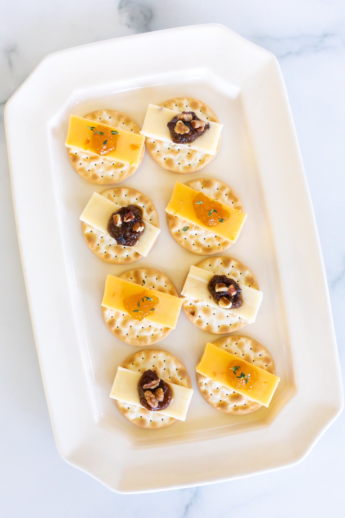 cheese and crackers topped with jelly on a white plate.