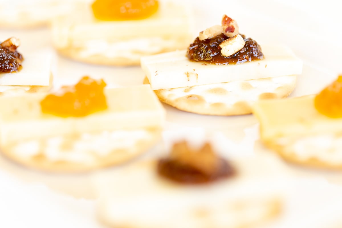 cheese and crackers topped with jelly on a white plate.