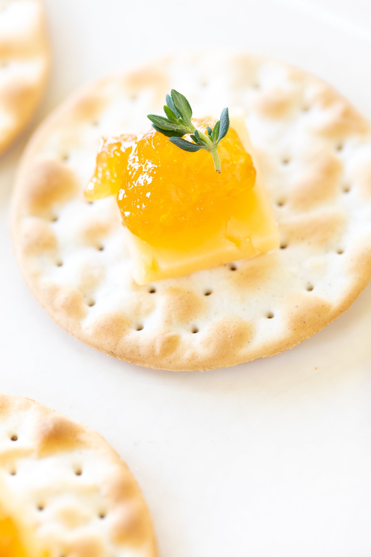 cheese and crackers topped with jelly on a white plate.