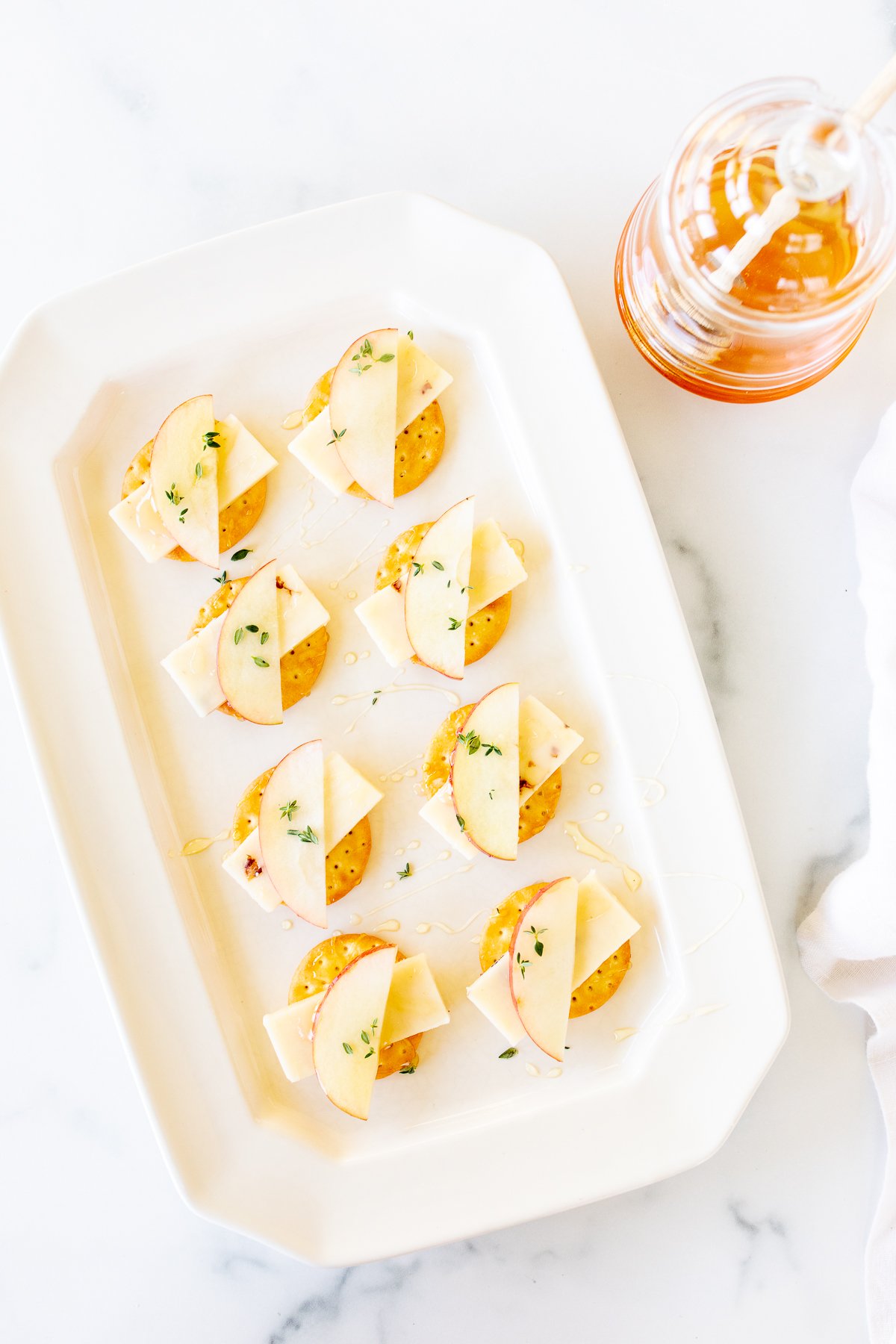 Cheese and crackers on a white platter, with an apple slice and fresh herbs.