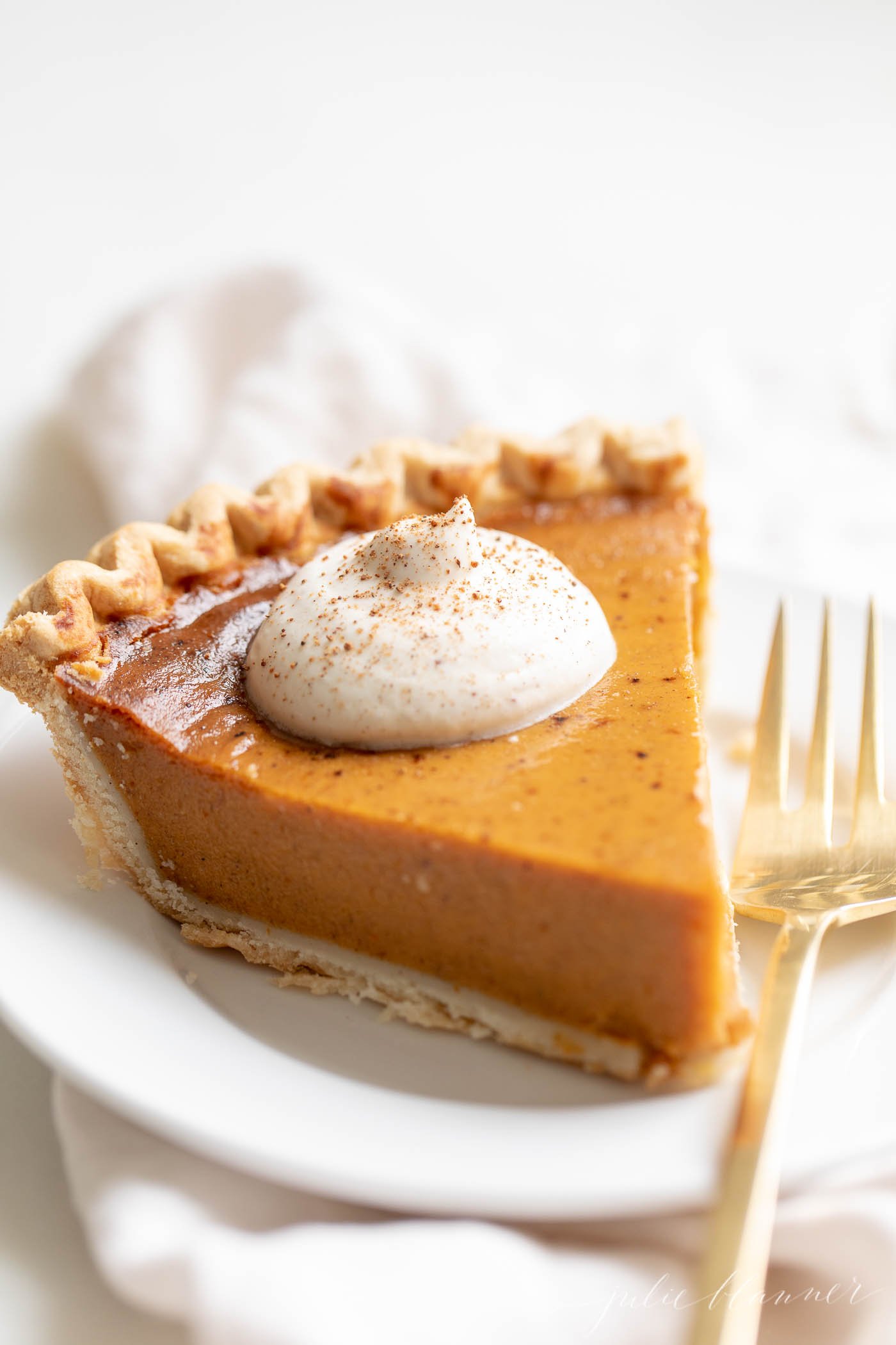 A slice of pumpkin pie with a dollop of eggnog whipped cream on top.