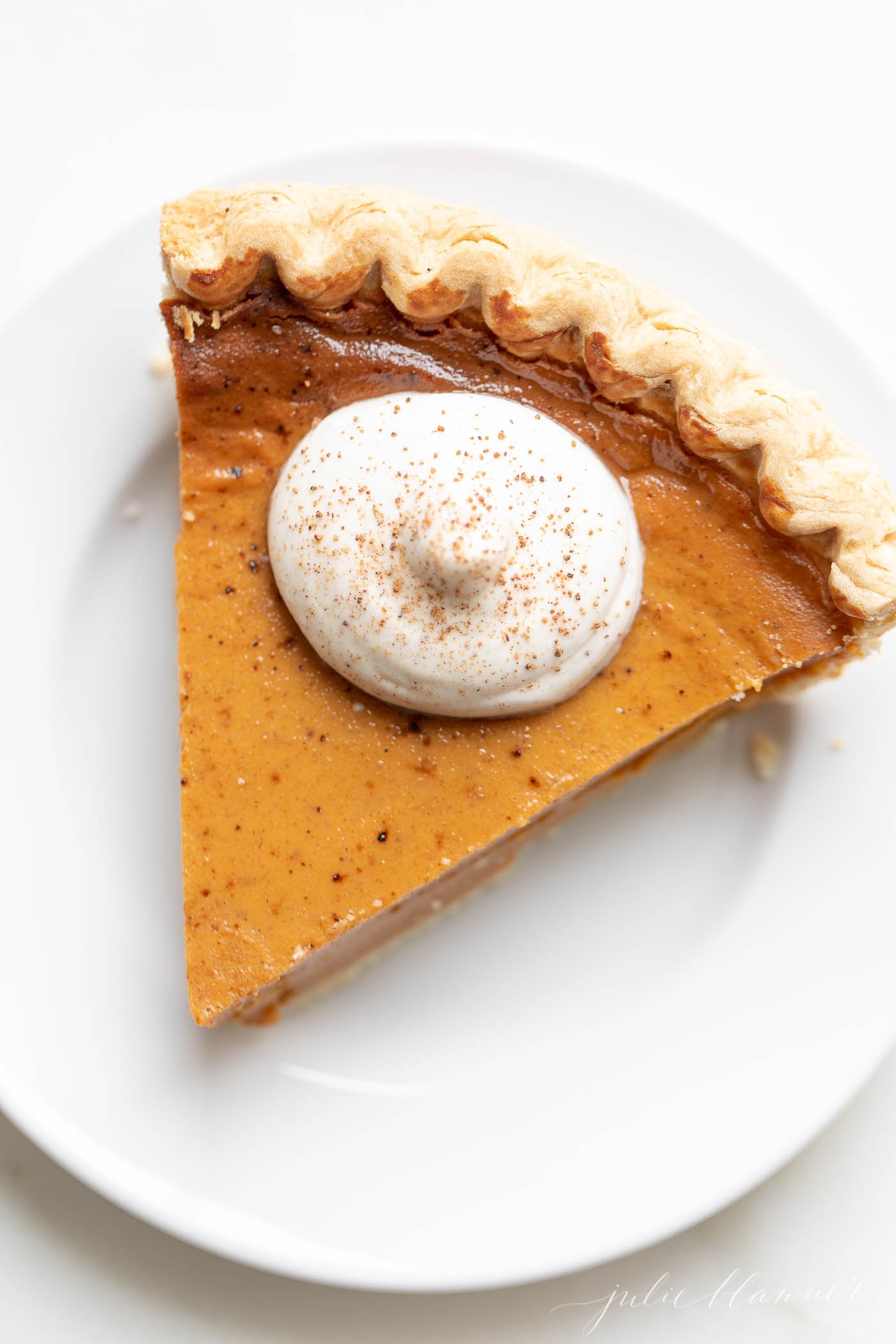 A slice of pumpkin pie with a dollop of eggnog whipped cream on top.