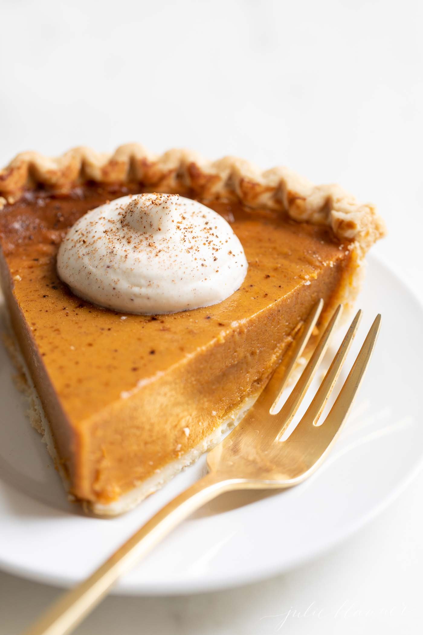 A slice of pumpkin pie with a dollop of eggnog whipped cream on top.