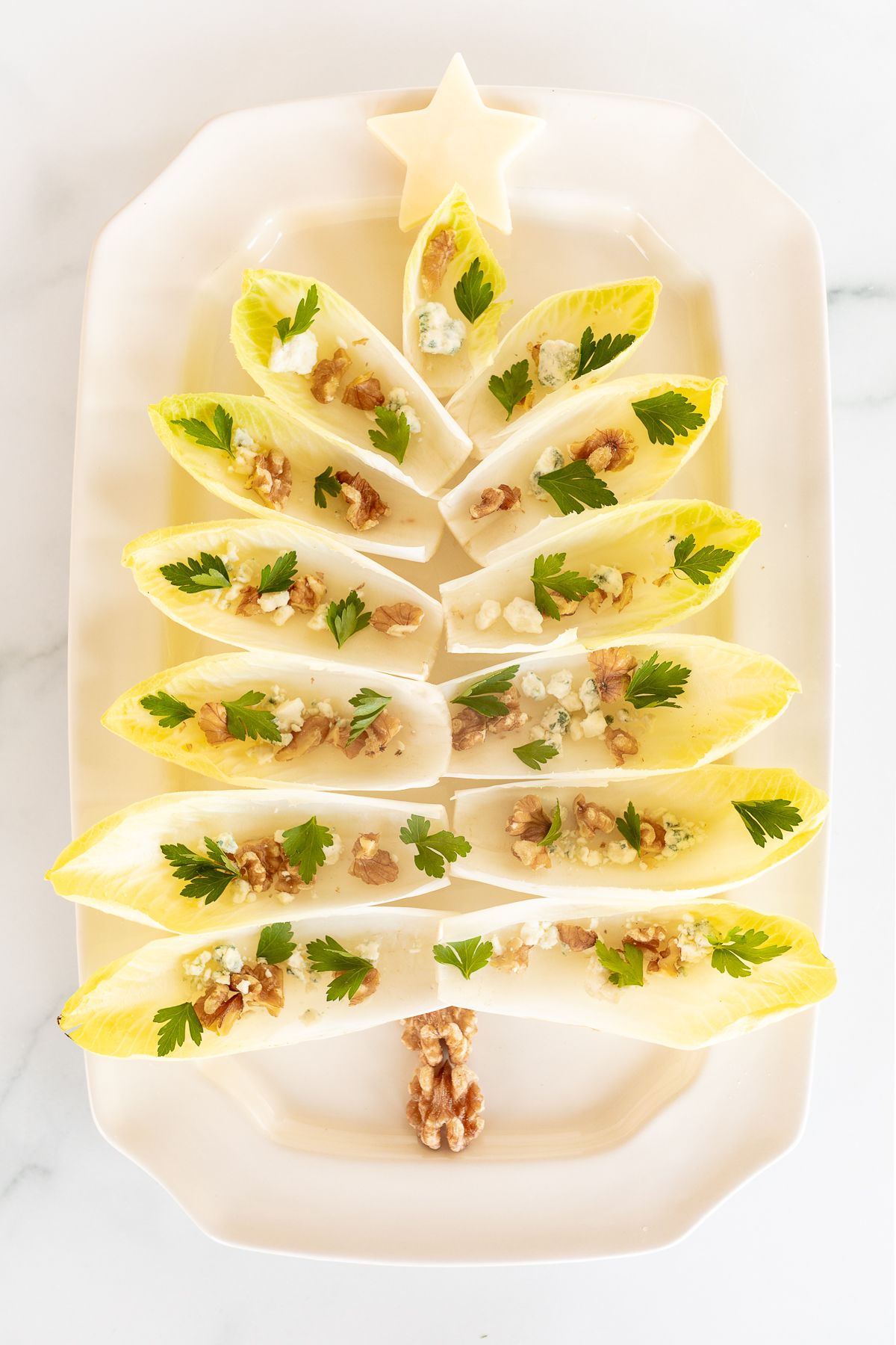 An endive salad laid out as a Christmas tree on a white platter.