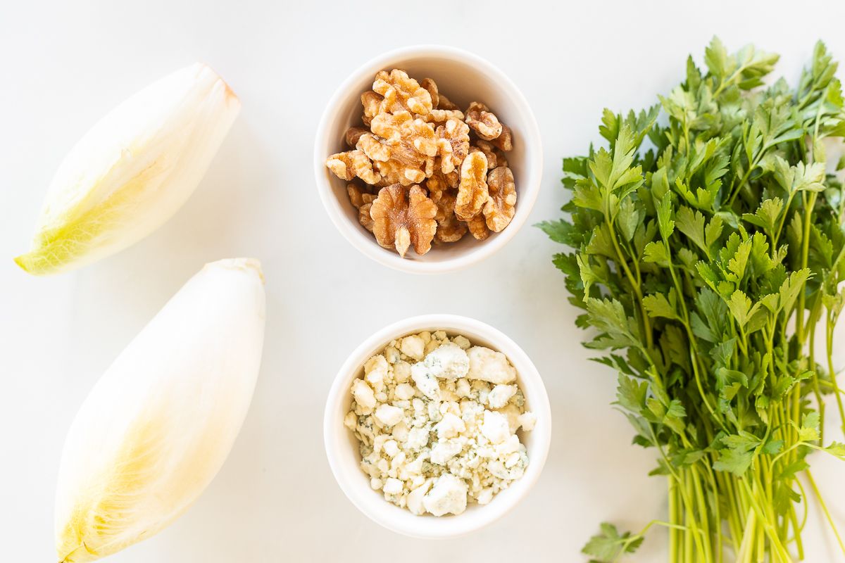 Ingredients for an endive salad laid out on a white surface.