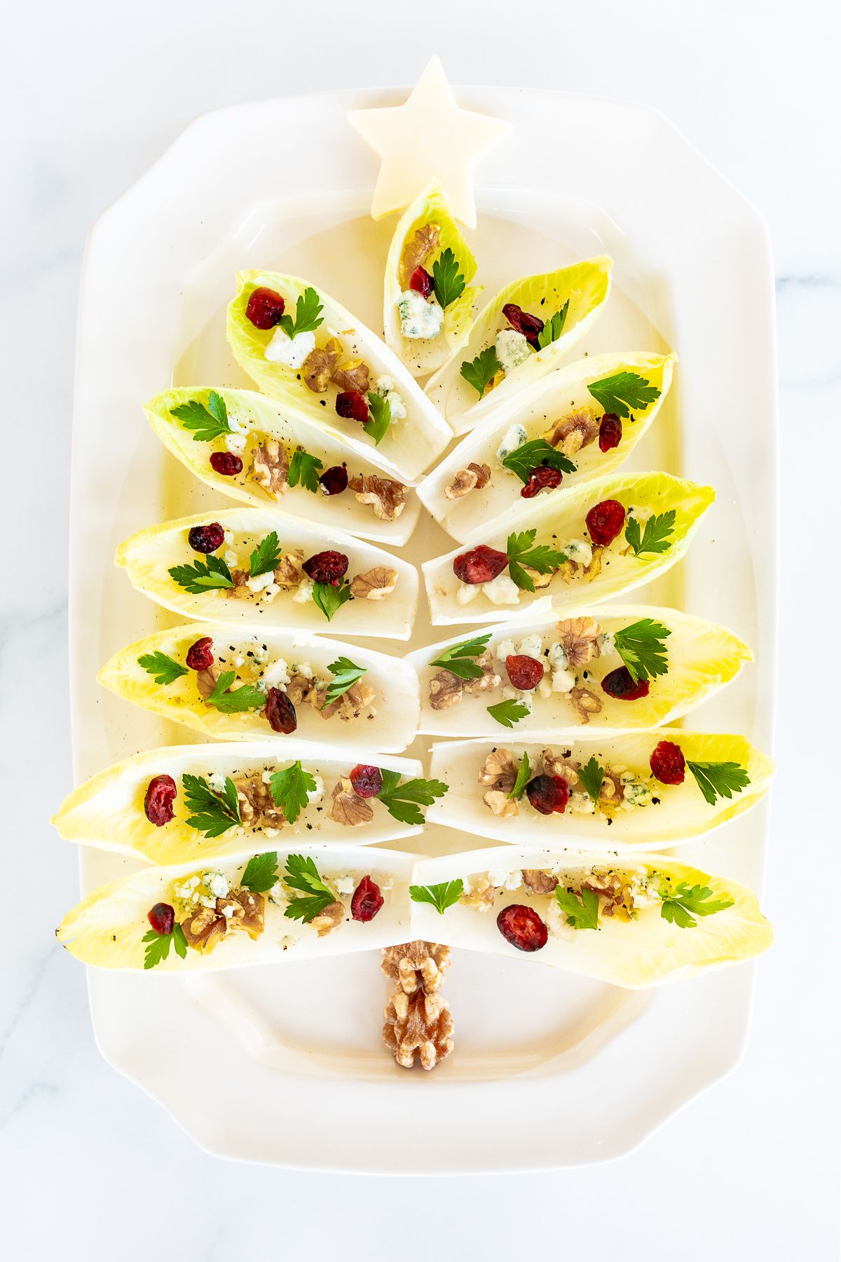 An endive salad laid out as a Christmas tree on a white platter.