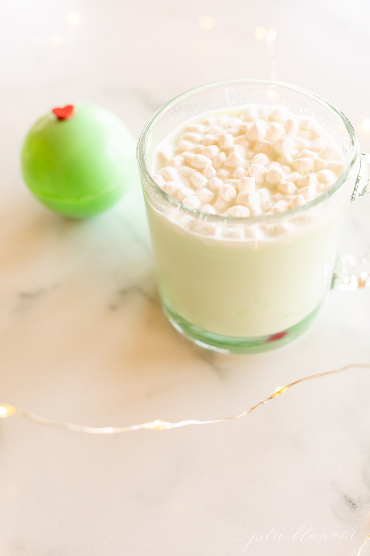 A cup of hot cocoa with whipped cream and a green Grinch hot chocolate bomb.