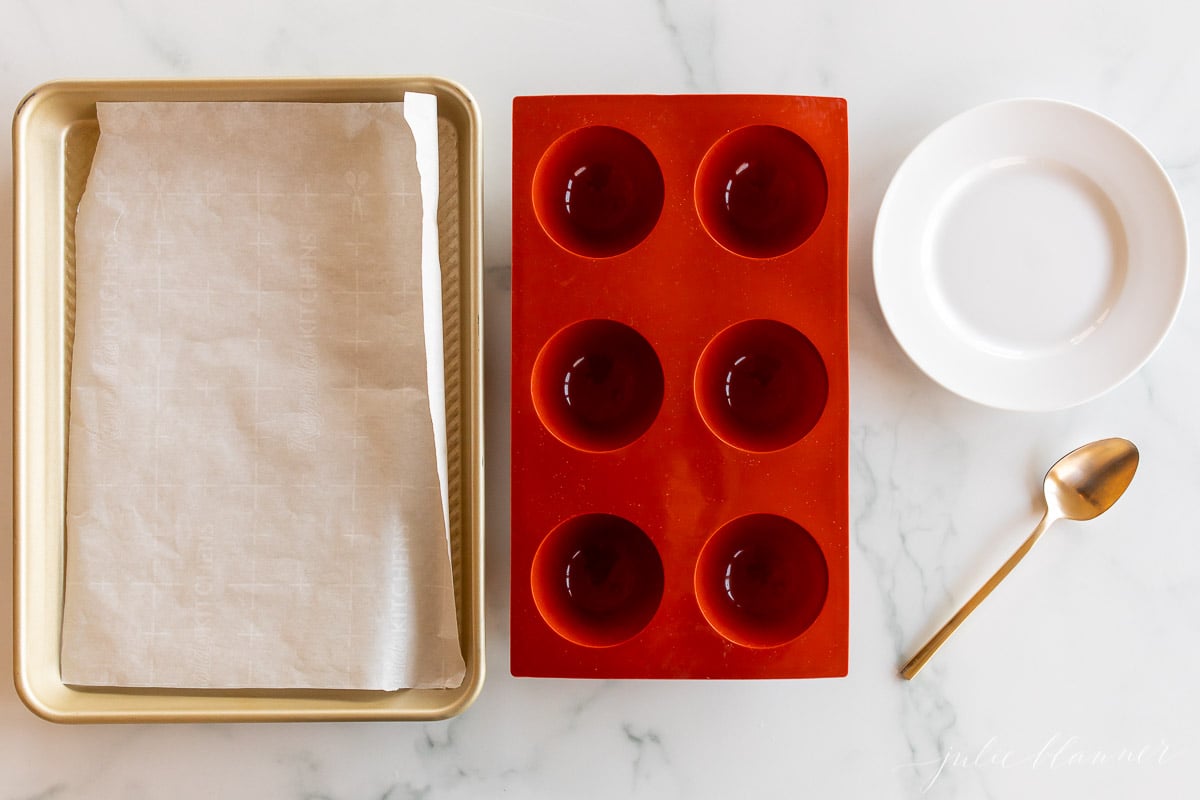 A red baking pan with a spoon next to it, used for making grinch hot chocolate bombs.