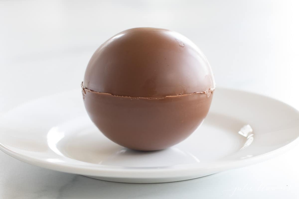 A white plate with a single Mexican hot chocolate bomb drizzled in cayenne pepper and chocolate.