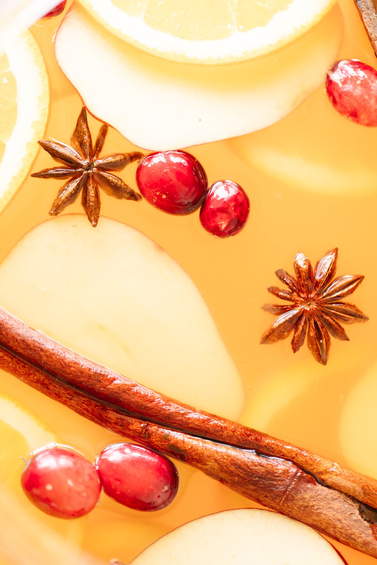 A close up of apple cider sangria with floating spices, cinnamon sticks and cranberries.