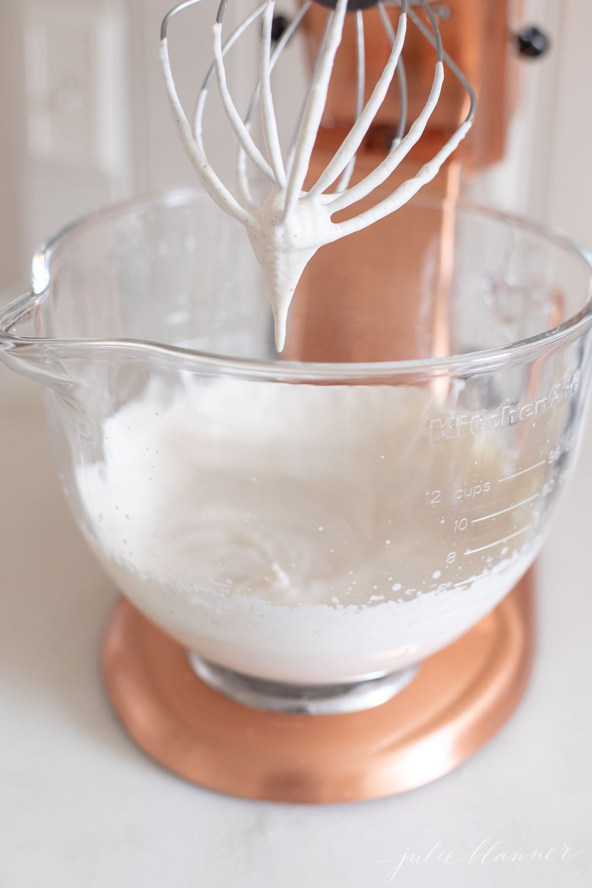 Eggnog whipped cream in the glass bowl of a copper stand mixer.