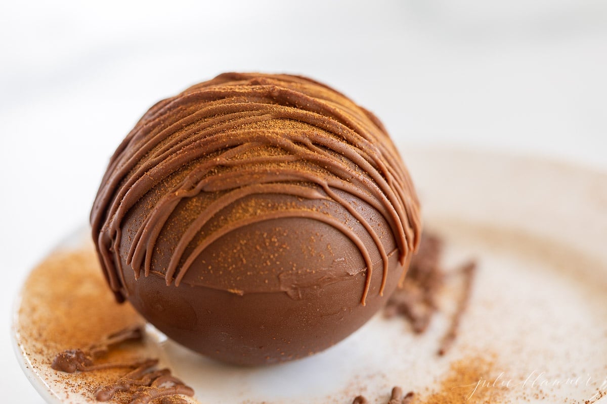A white plate with a single Mexican hot chocolate bomb drizzled in cayenne pepper and chocolate.