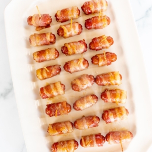 A white tray with bacon wrapped little smokies.