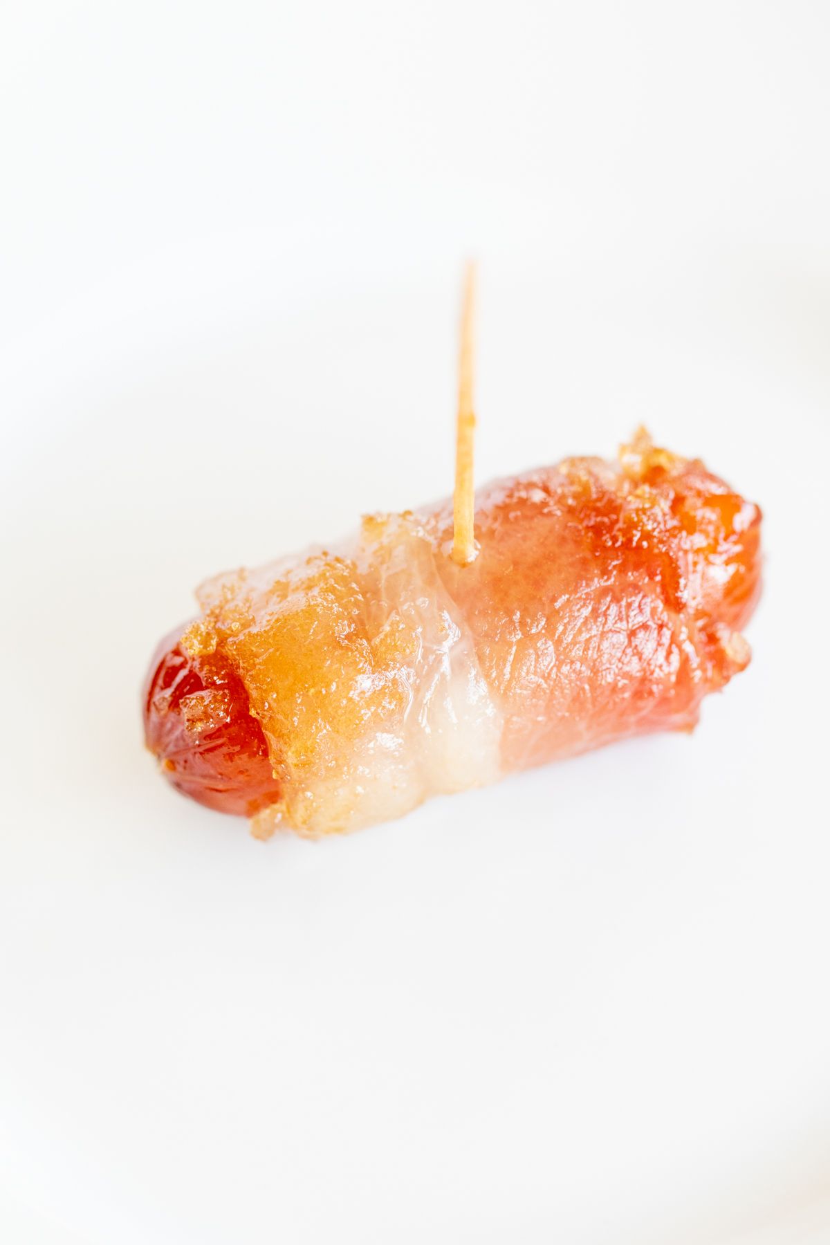 A single bacon wrapped little smokie on a white plate.