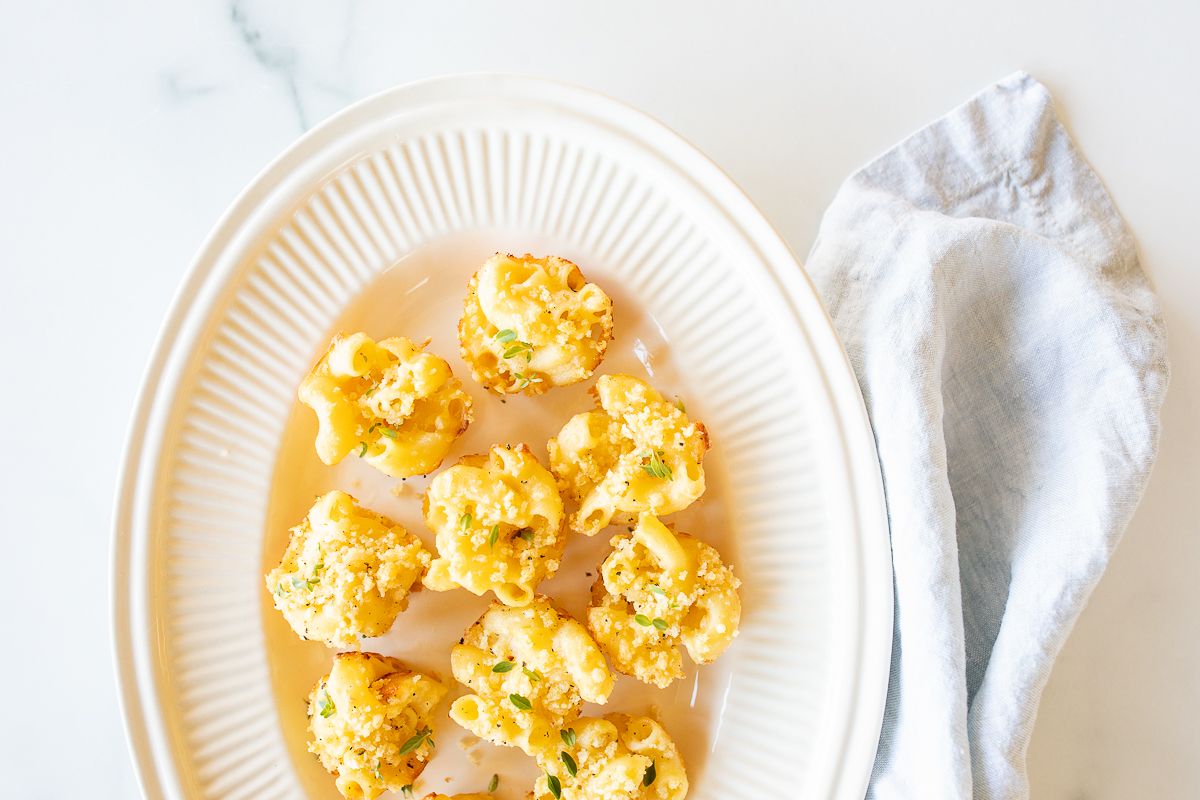 A white oval platter full of mini mac and cheese cups for an appetizer.