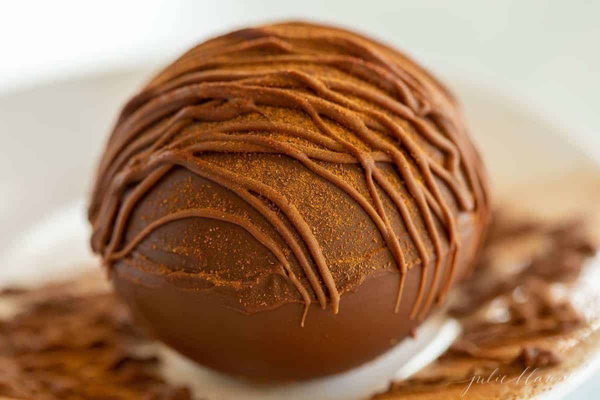 A white plate with a single Mexican hot chocolate bomb dusted in cayenne pepper and chocolate.