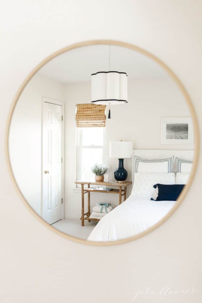 A white guest room with blue accents through the reflection in a brass mirror.