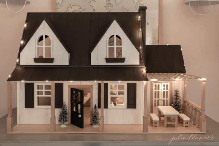 A little girls' room with bunk beds and a blue chest of drawers topped with a dollhouse decorated for Christmas.