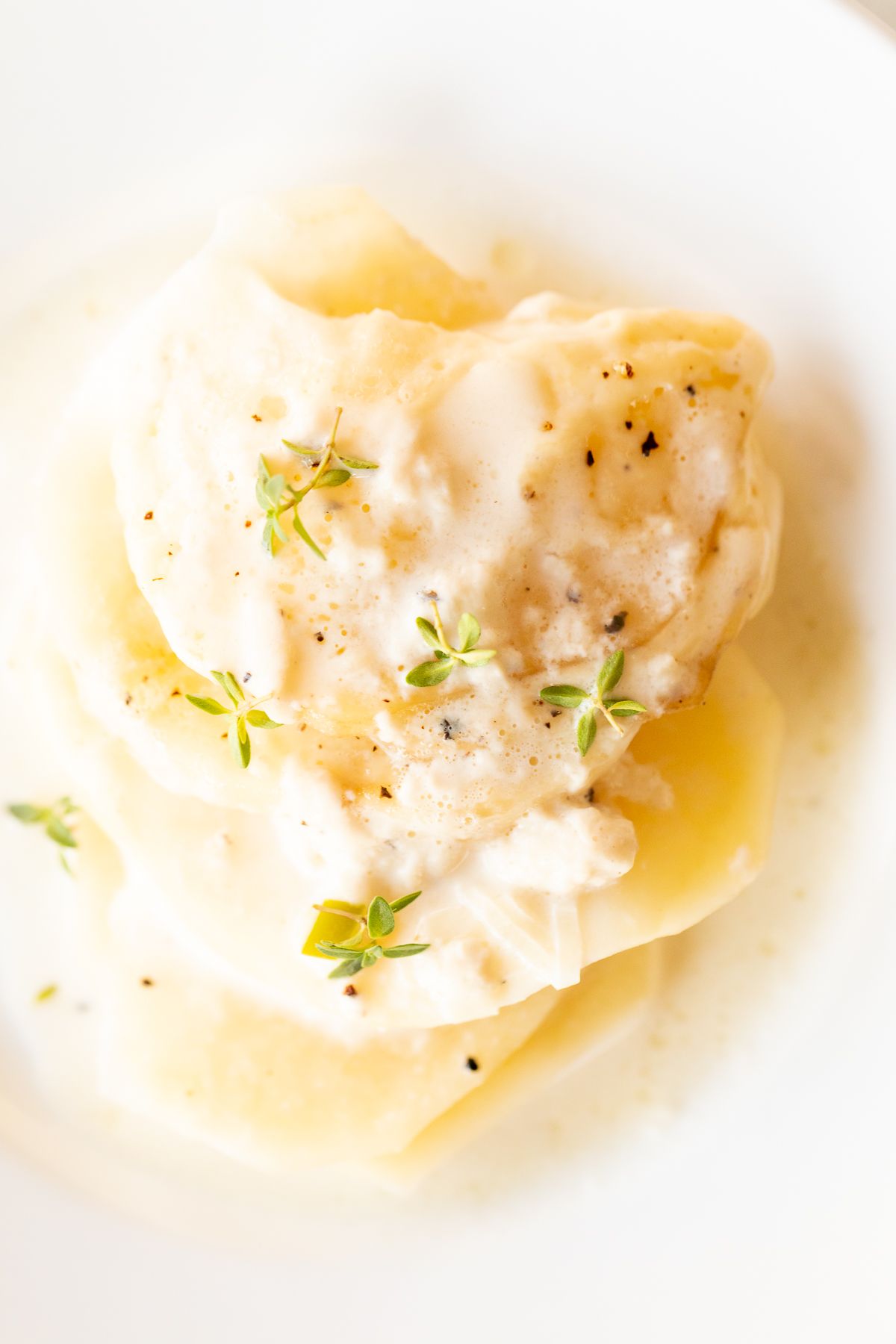 A white plate featuring potato gratin stacks, garnished with fresh thyme.