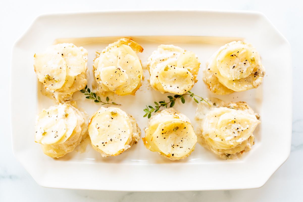 A white platter featuring potato gratin stacks, garnished with fresh thyme.