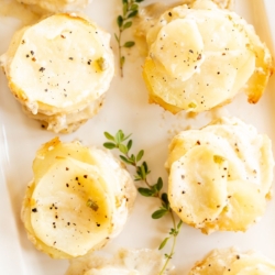 A white platter featuring potato gratin stacks, garnished with fresh thyme.