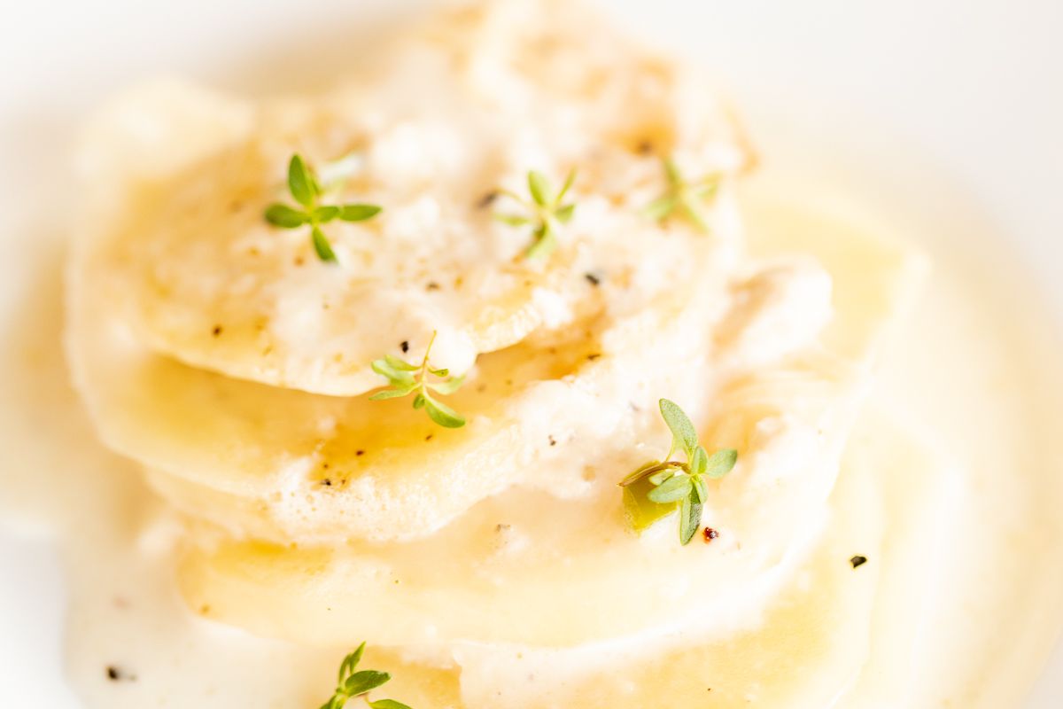 A white plate featuring potato gratin stacks, garnished with fresh thyme.