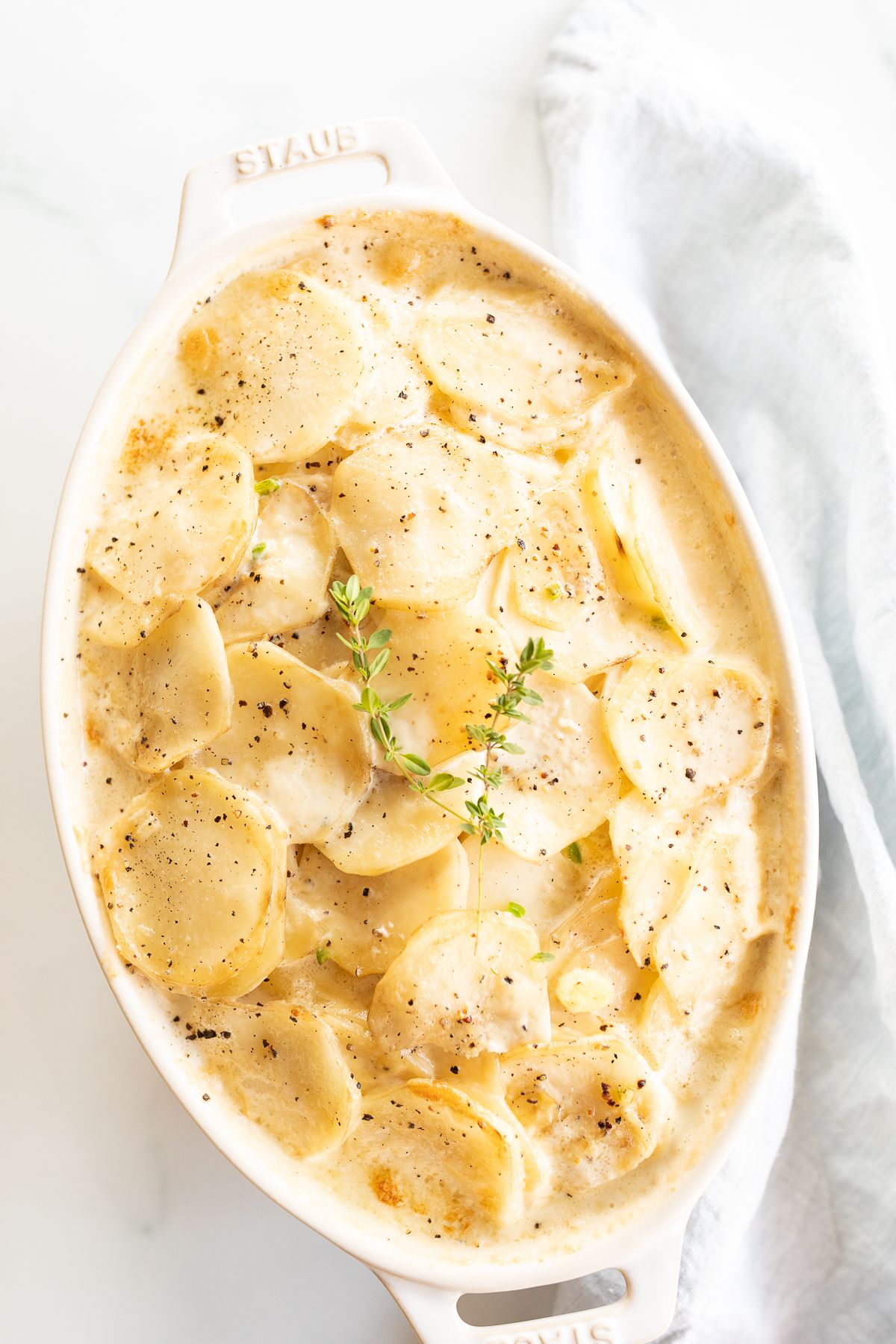 Gratin Dauphinoise potatoes in a white oval baking dish, garnished with fresh thyme.