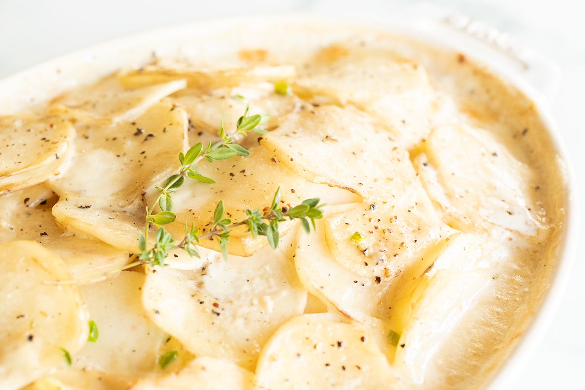 Gratin potatoes in a white oval baking dish, garnished with fresh thyme.