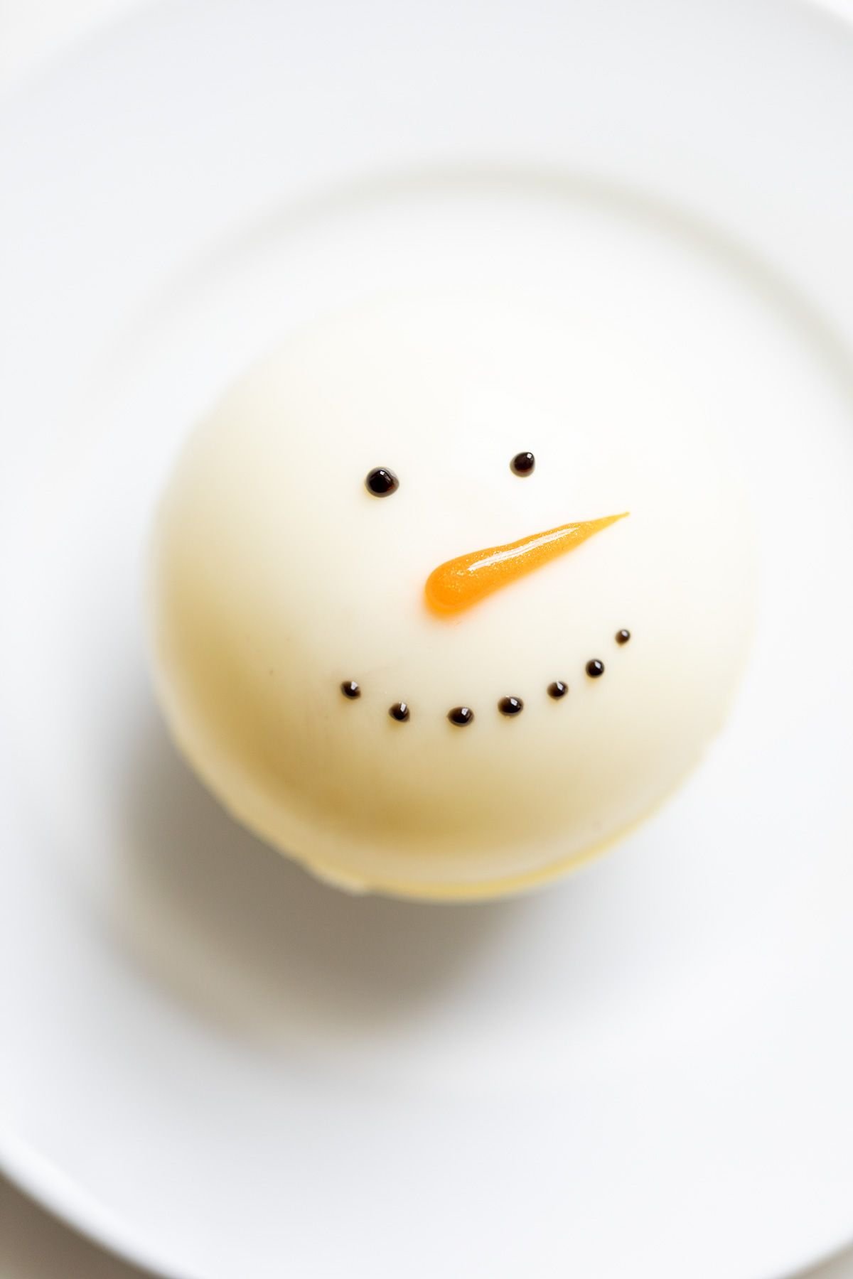 A snowman hot chocolate bomb on a white plate.