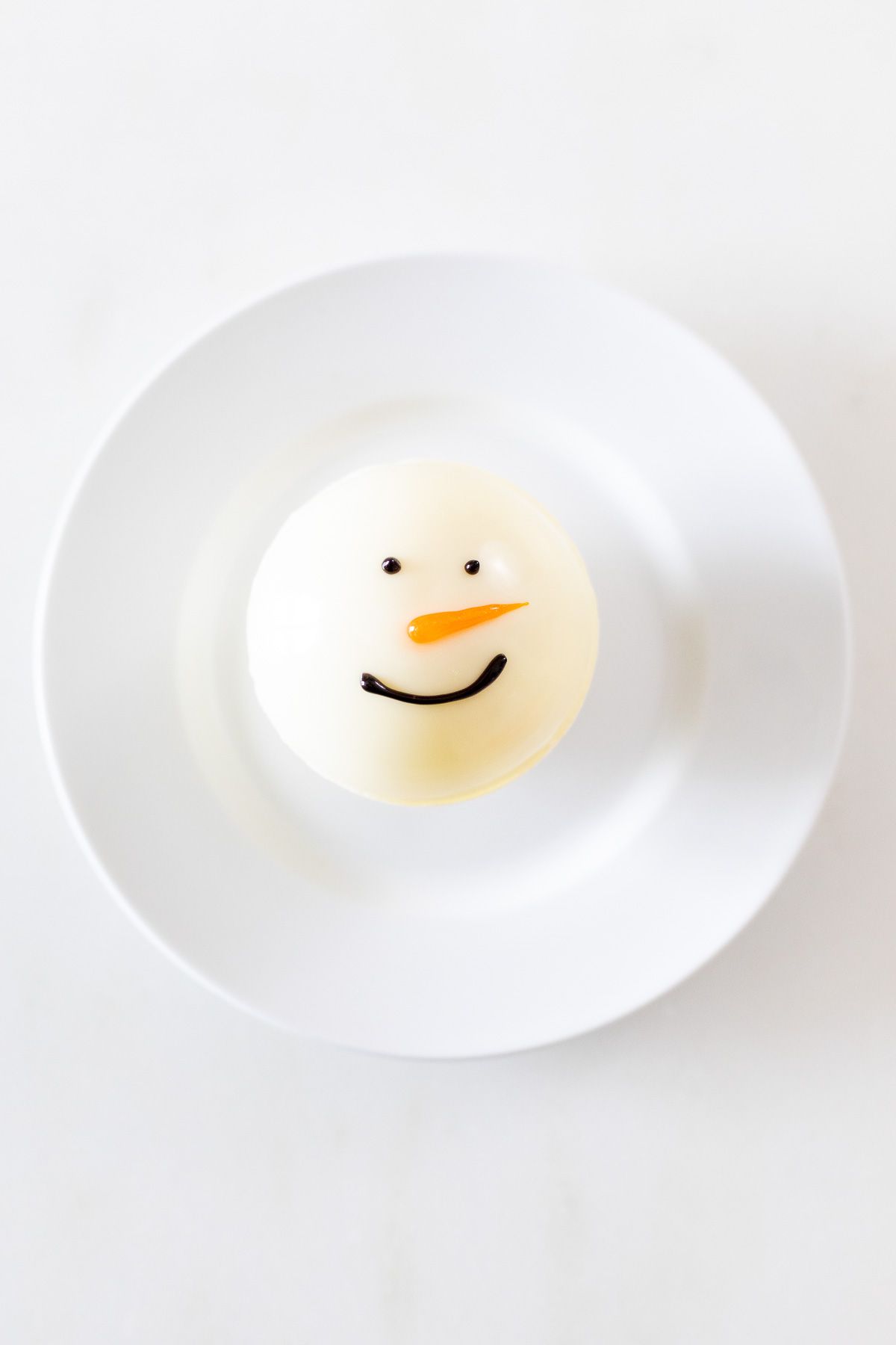 A snowman hot chocolate bomb on a white plate.