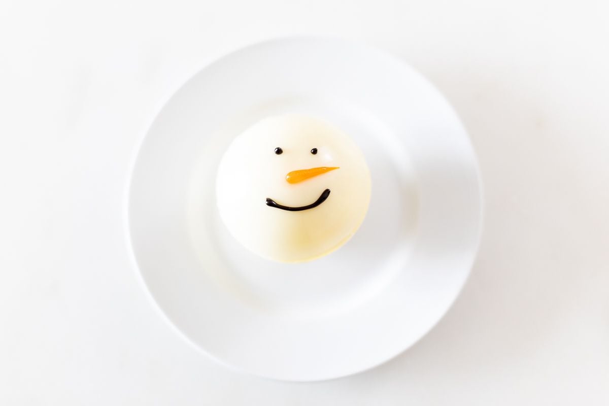 A snowman hot chocolate bomb on a white plate.