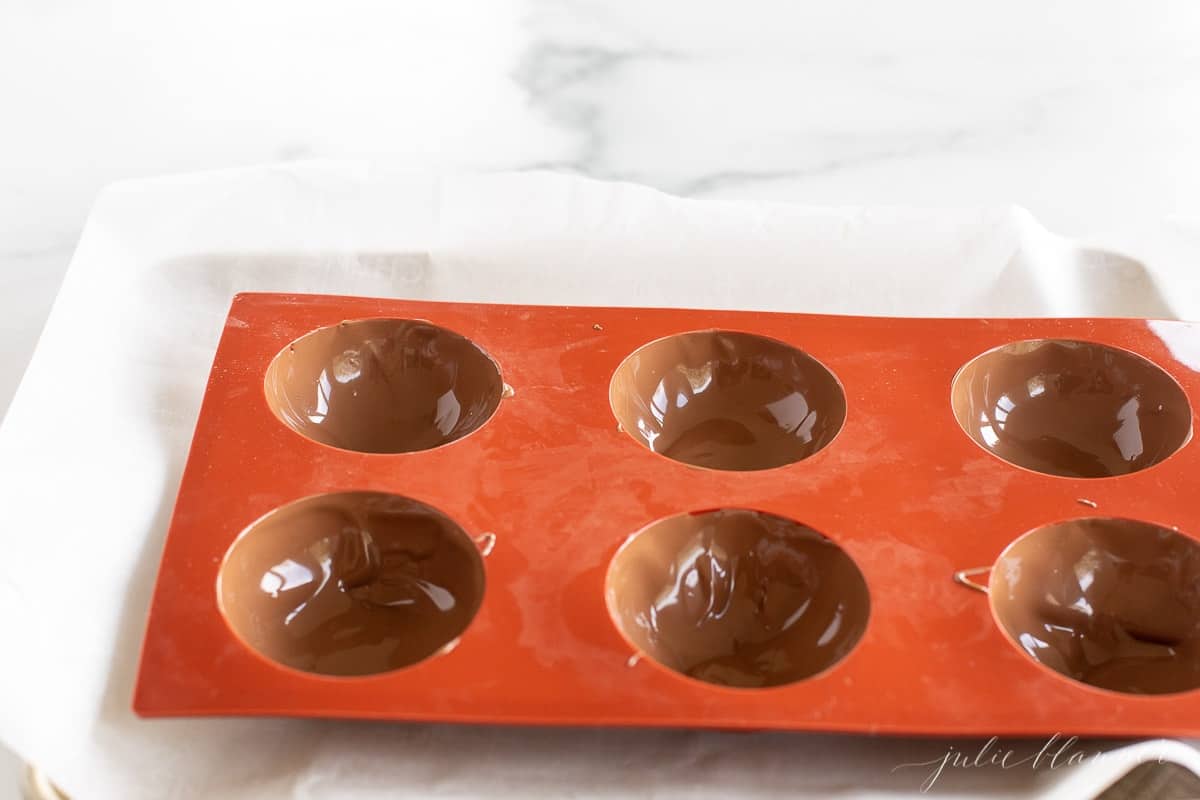 A red silicone sphere mold filled with chocolate for Mexican hot chocolate bombs.