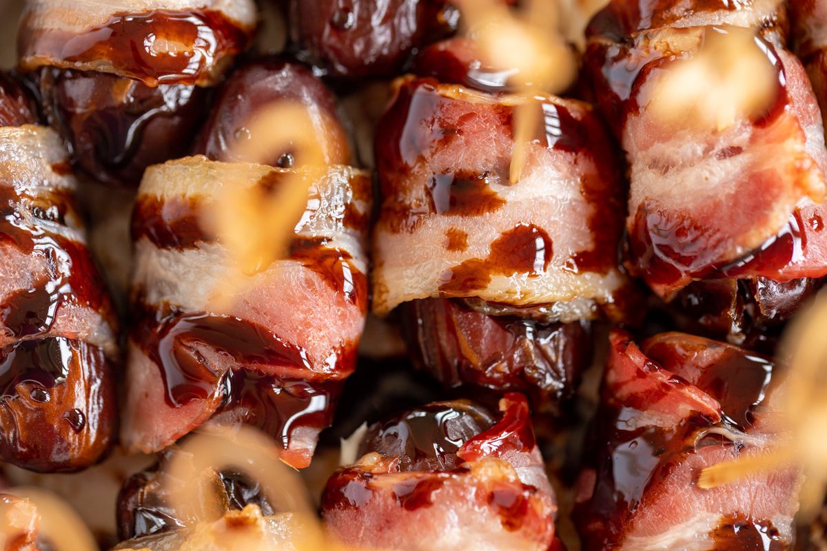 A close up of stuffed dates wrapped in bacon and drizzled in balsamic glaze.