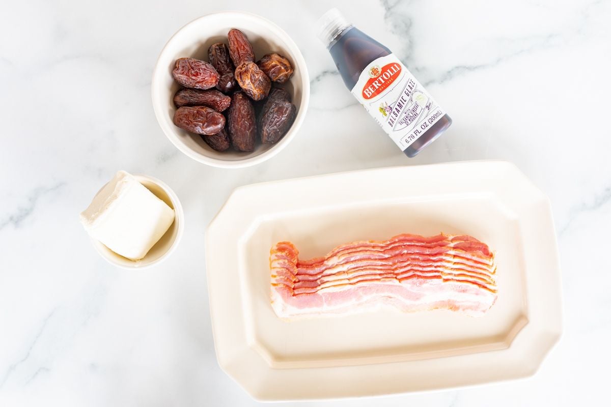 Ingredients for bacon wrapped dates laid out on a marble countertop.