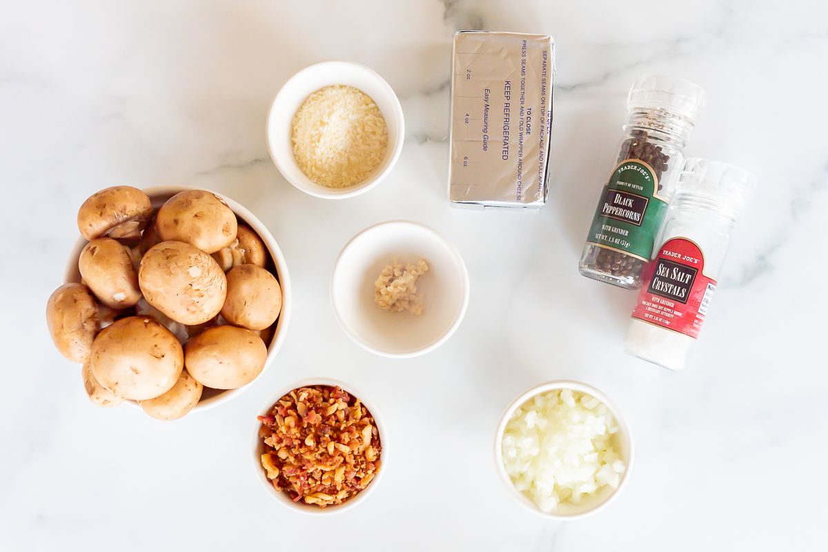 Ingredients for cream cheese and bacon stuffed mushrooms laid out on a marble countertop.