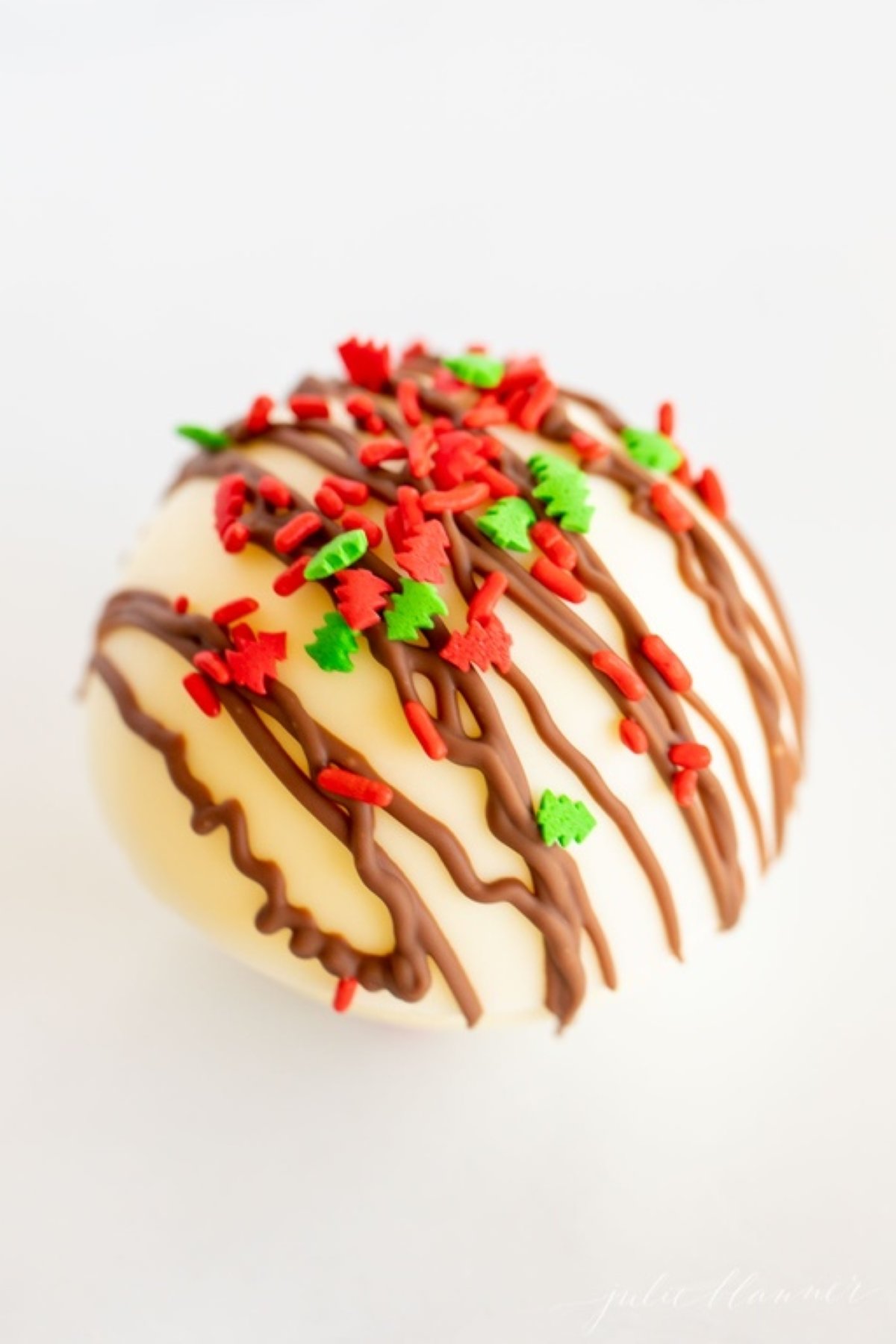 A white chocolate hot chocolate bomb, covered in red and green sprinkles.