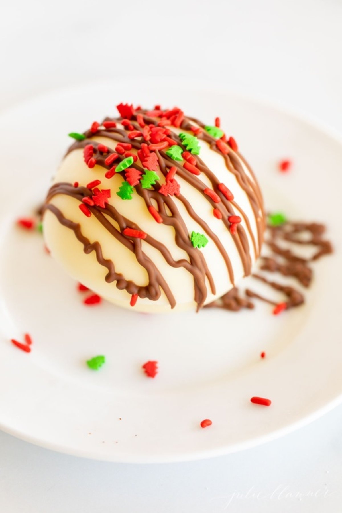 A white chocolate hot chocolate bomb, covered in red and green sprinkles.
