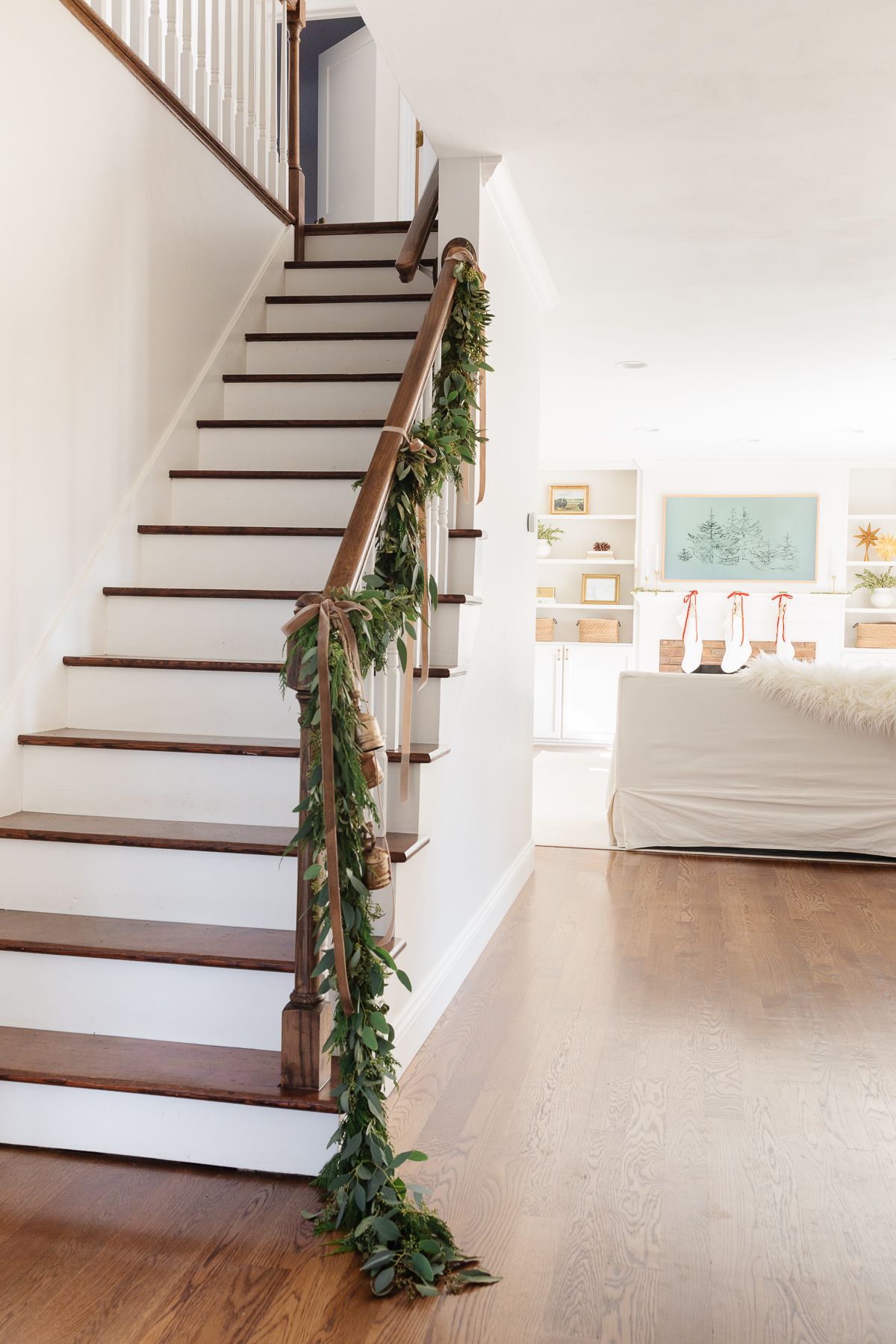 Fresh Christmas garlands on a stairwell in a white entryway of a home.