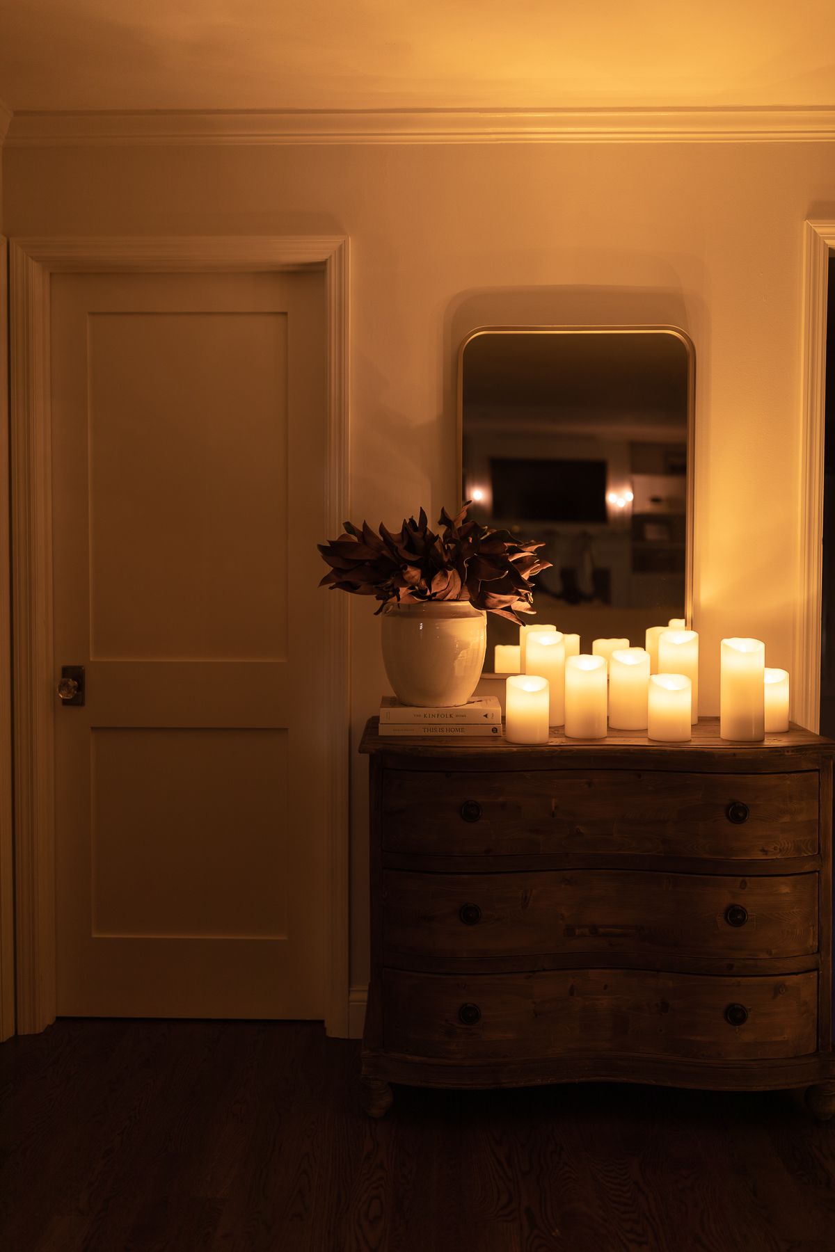 An entry table with a vase of magnolia and christmas lights in the background.