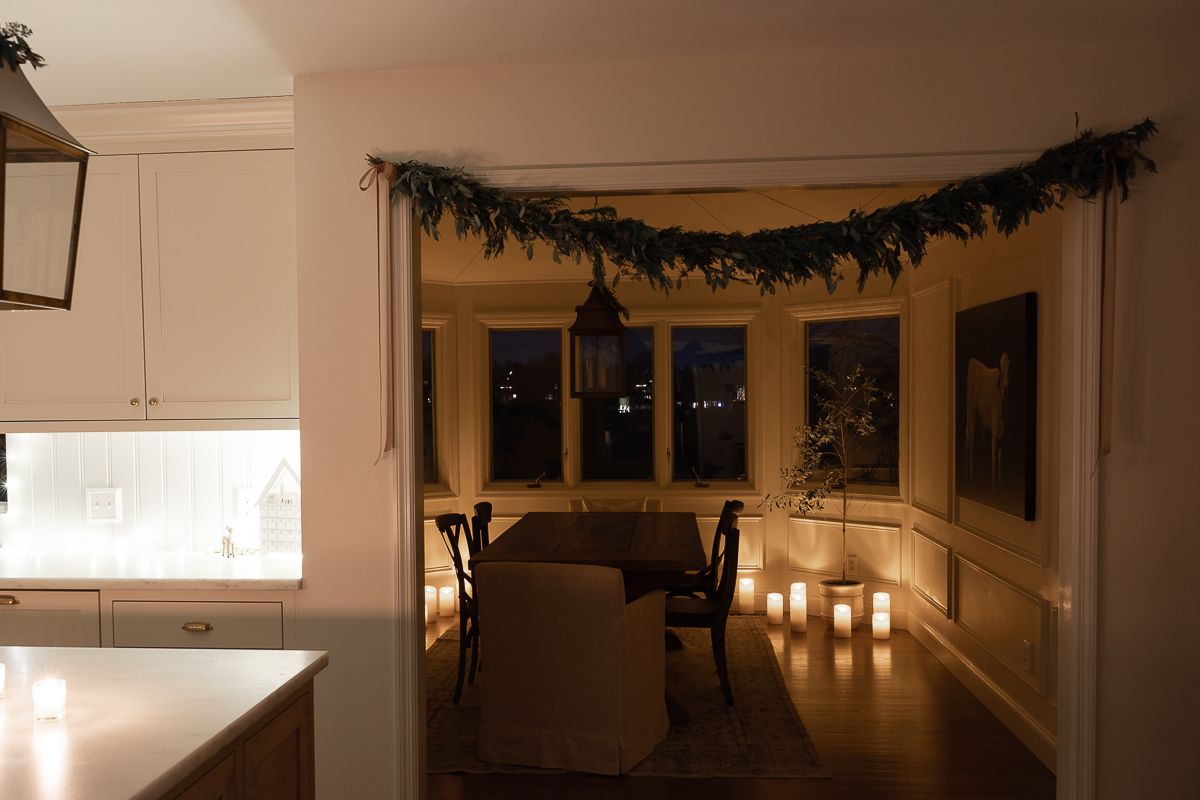 A dining room with candle light and a garland hanging over the doorway for Christmas