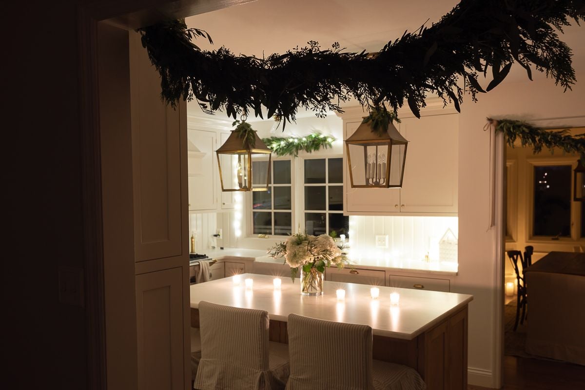 A white kitchen with Christmas flowers and candles on the island at night
