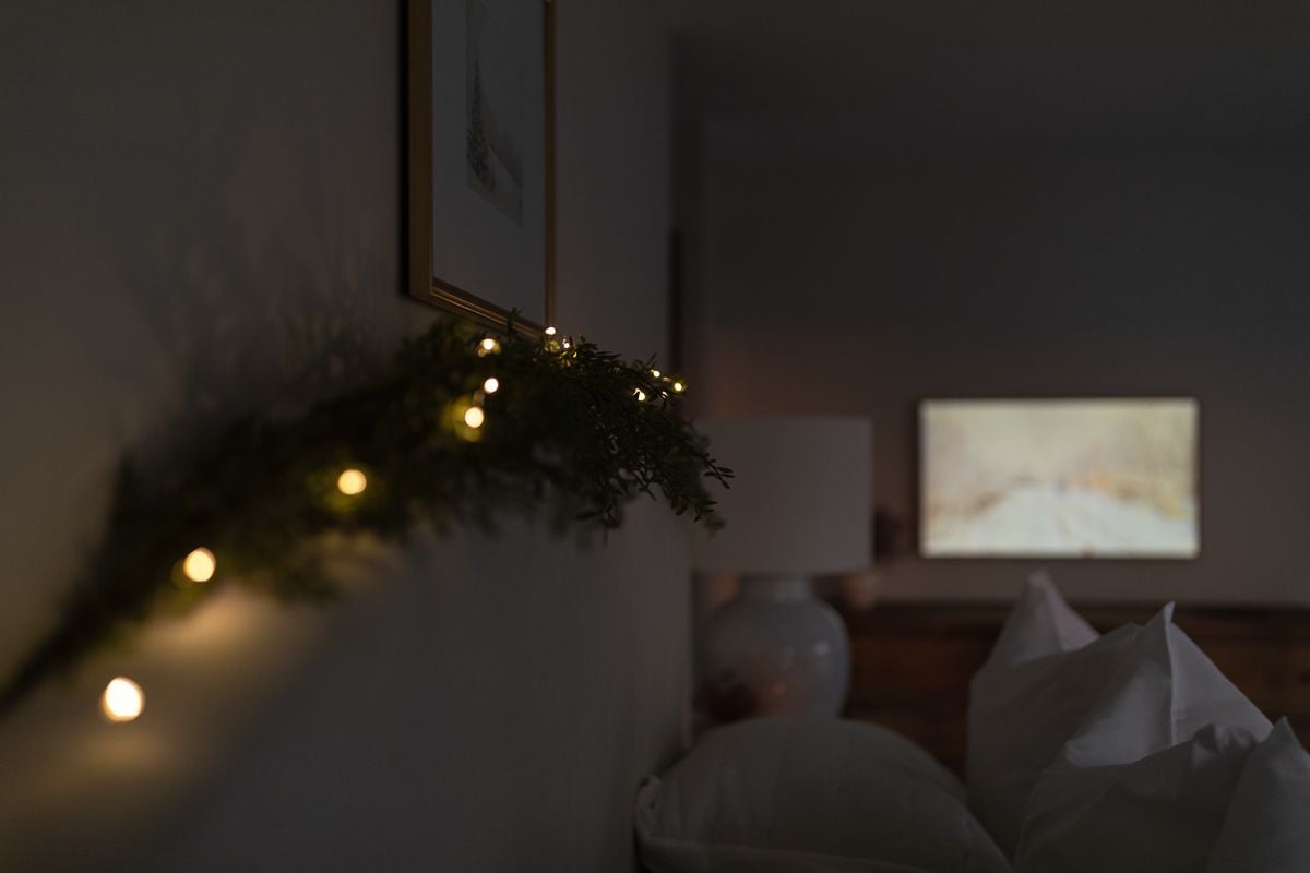 A white bed with a garland and lights over it for Christmas.